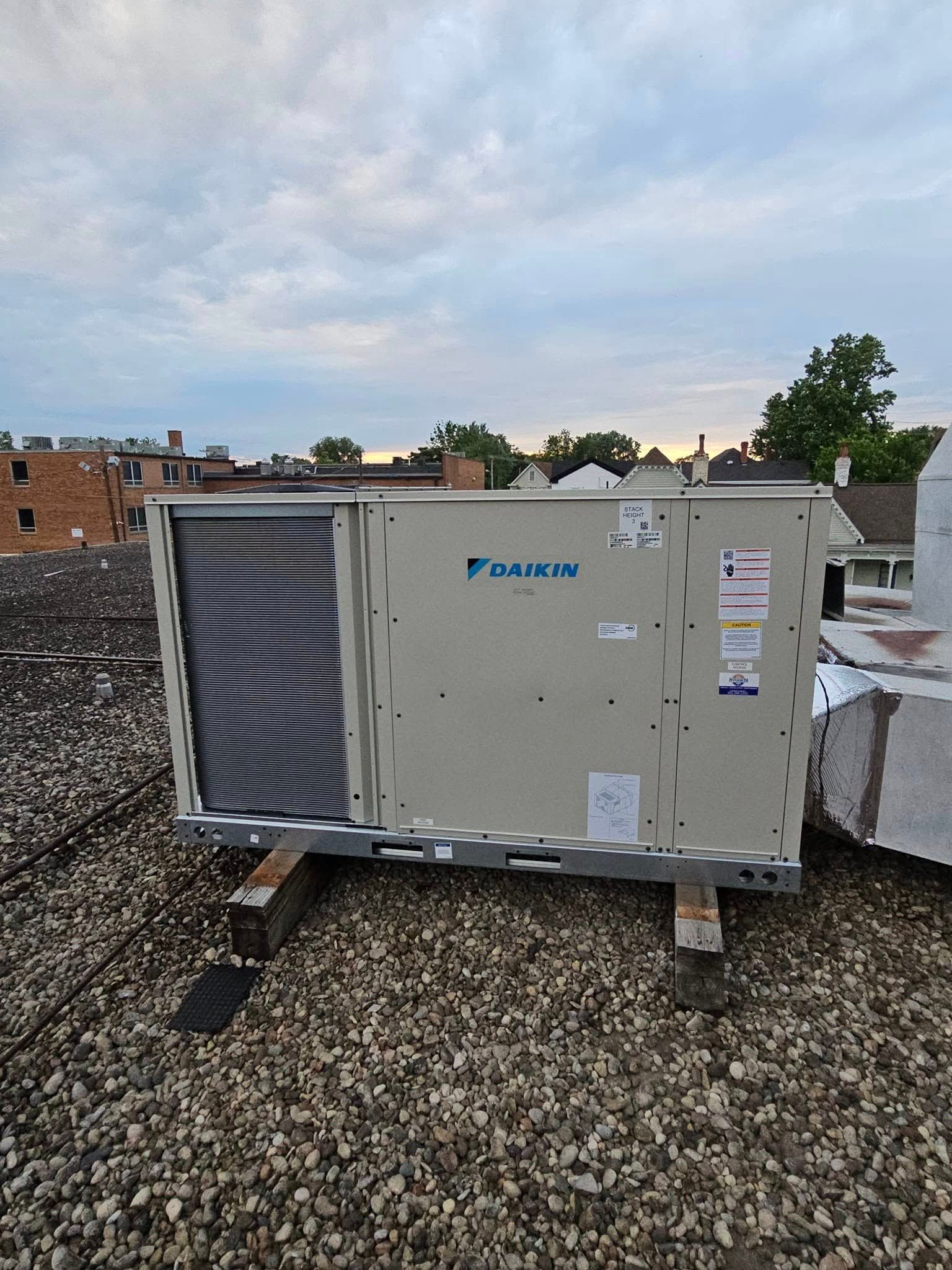 A large air conditioner is sitting on top of a gravel roof.