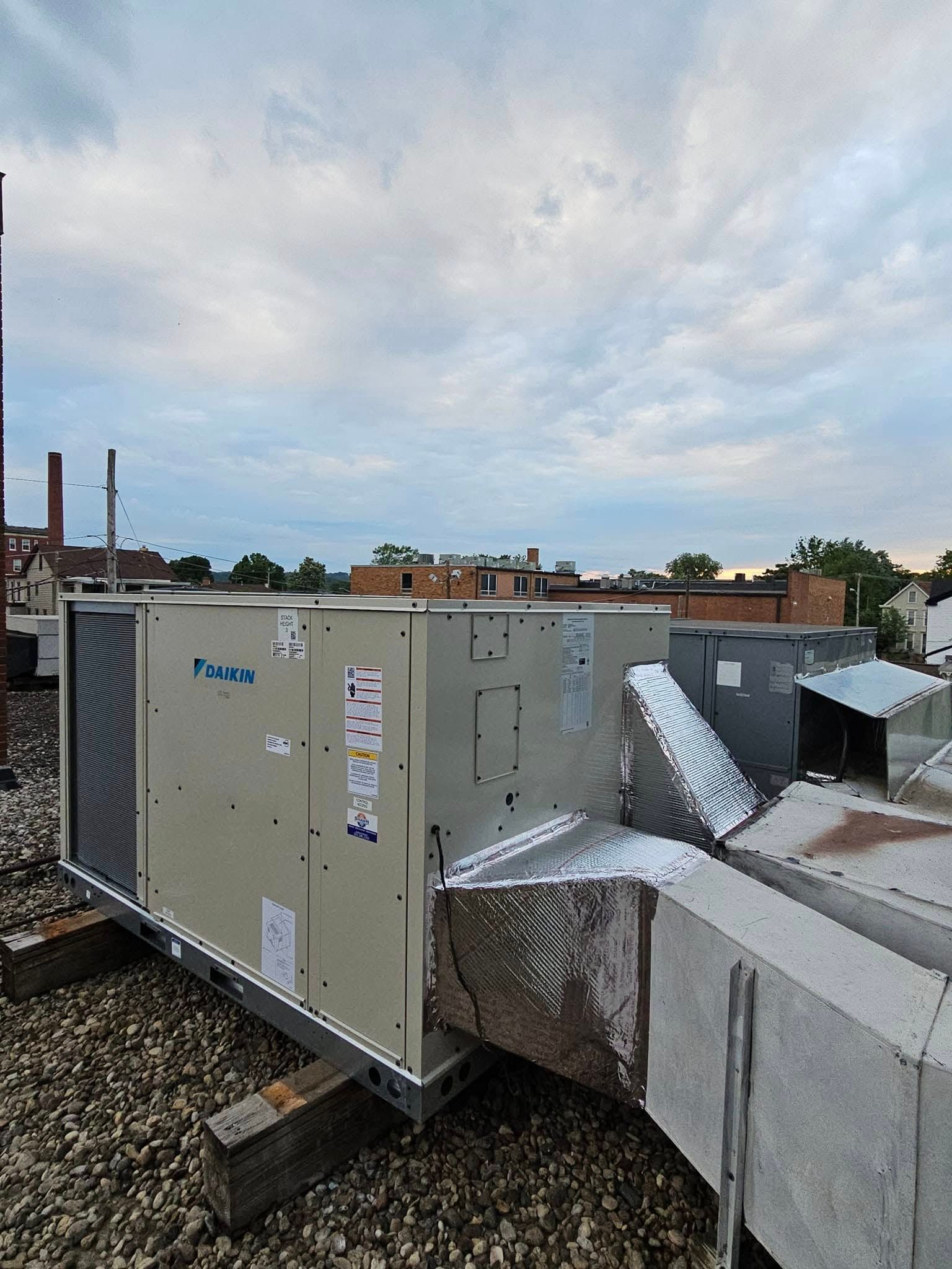 A large air conditioner is sitting on top of a gravel covered roof.