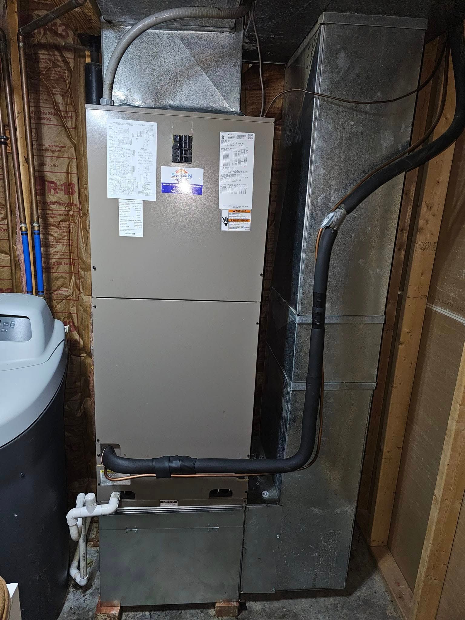 An air conditioner is sitting in a basement next to a trash can.