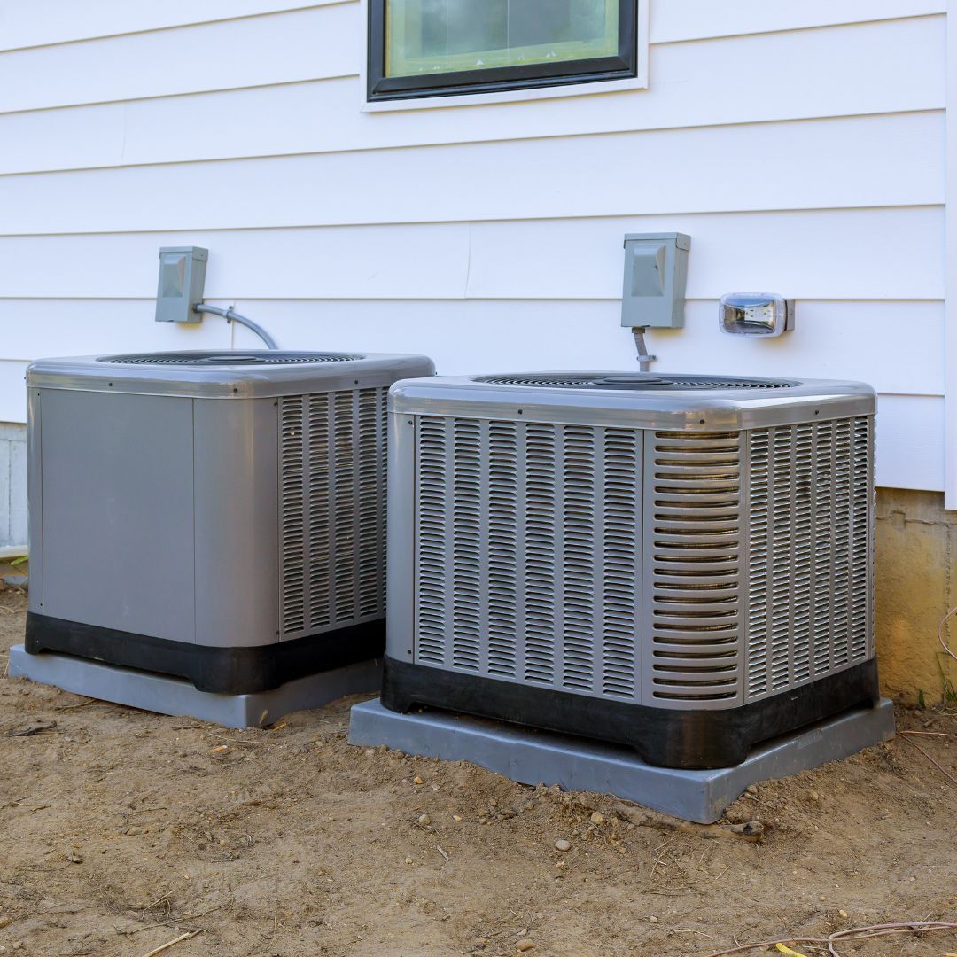 Two air conditioners are sitting outside of a house
