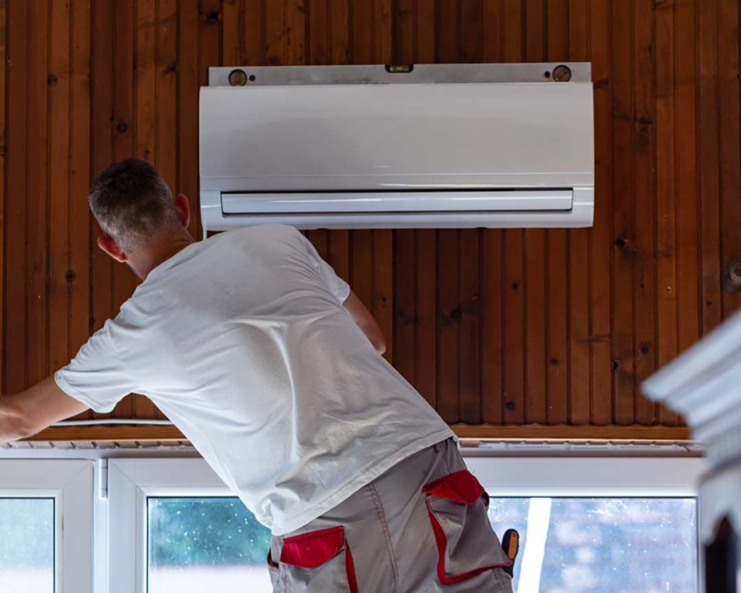 A man is installing an air conditioner on a wooden wall.