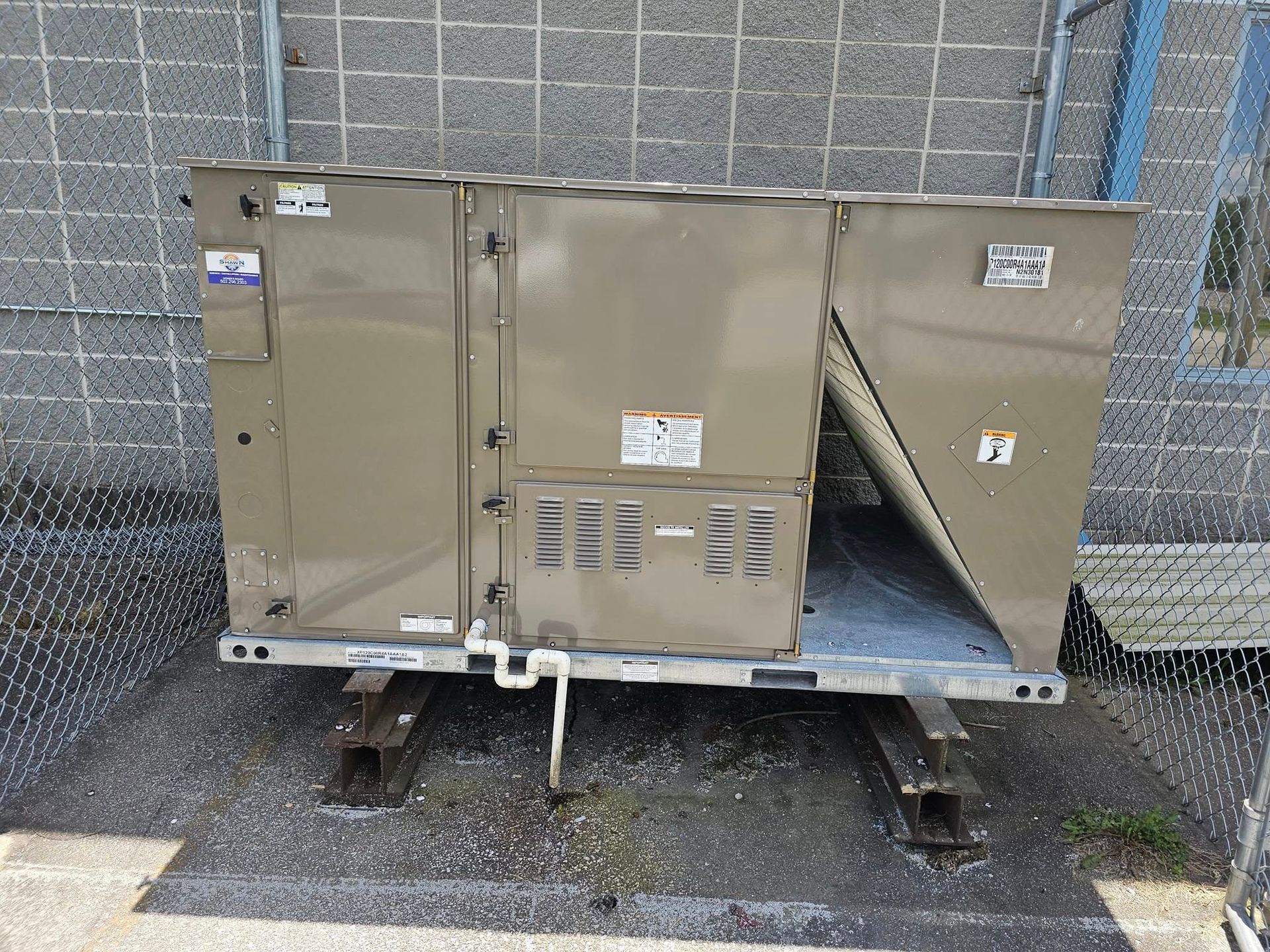 A large stainless steel air conditioner is sitting on the ground in front of a building.