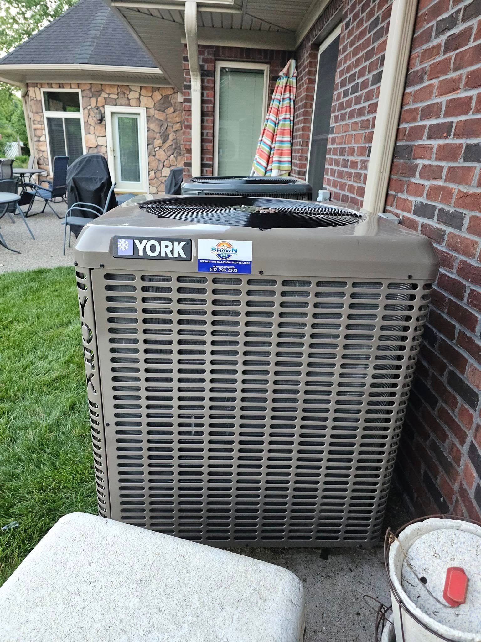 A york air conditioner is sitting on the side of a brick house.