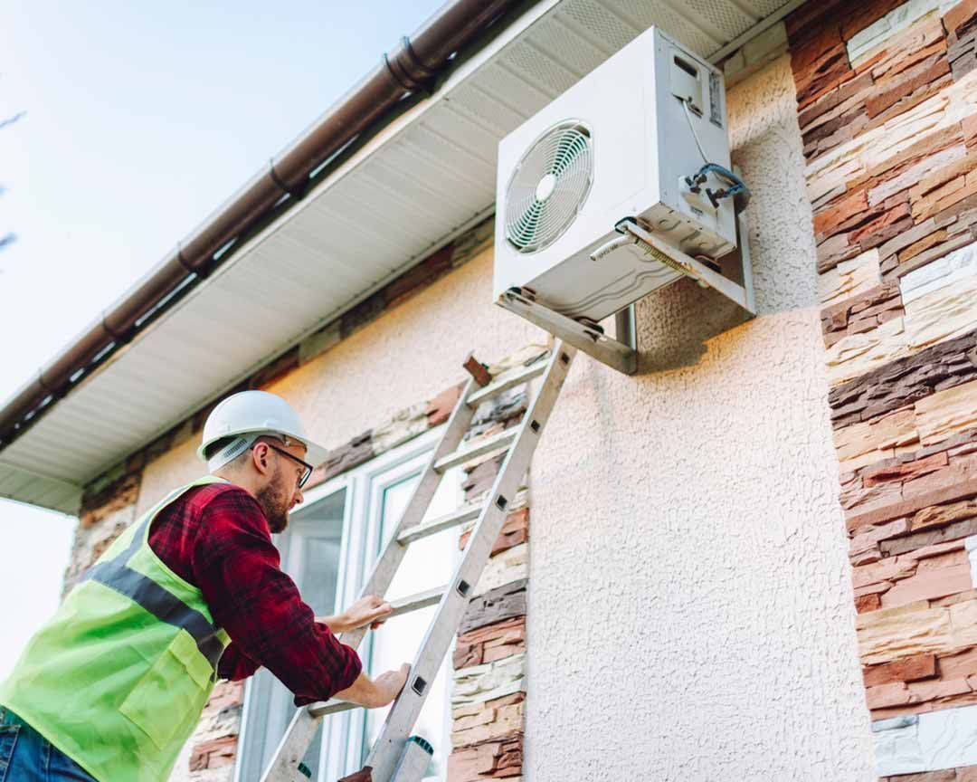 A man is climbing a ladder to install an air conditioner on the side of a building.
