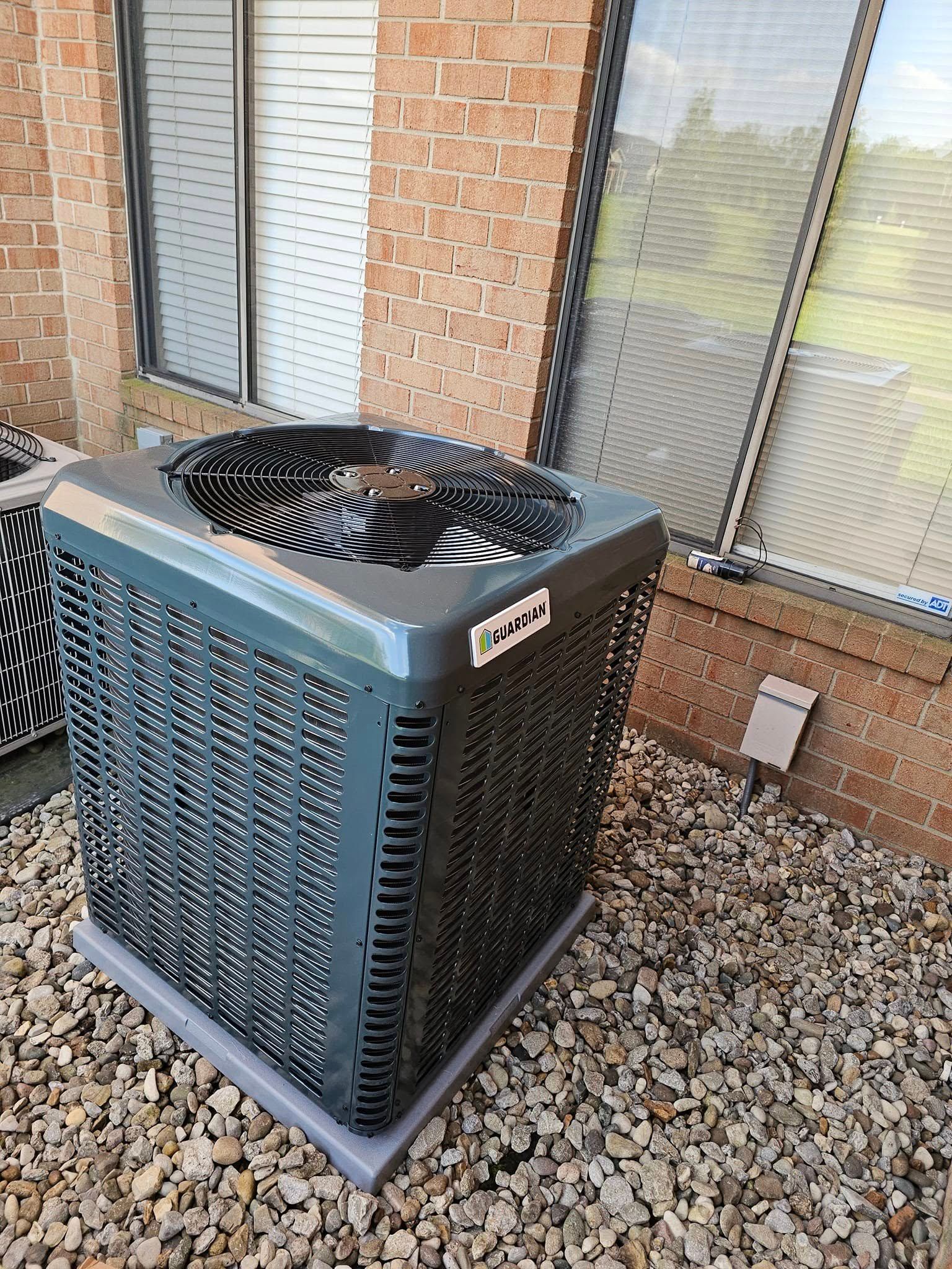 A large air conditioner is sitting on top of a pile of gravel in front of a brick building.