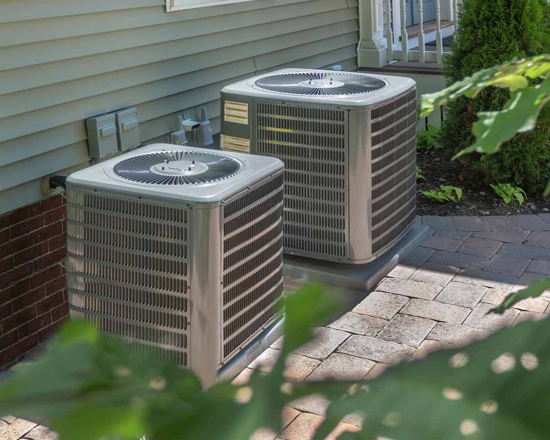 Two air conditioners are sitting on the side of a house.