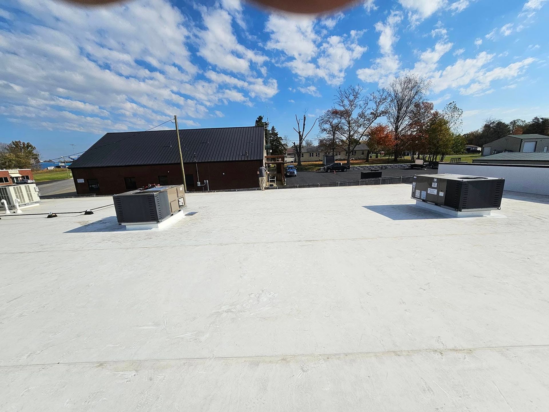 A white roof with a building in the background and a blue sky with clouds.