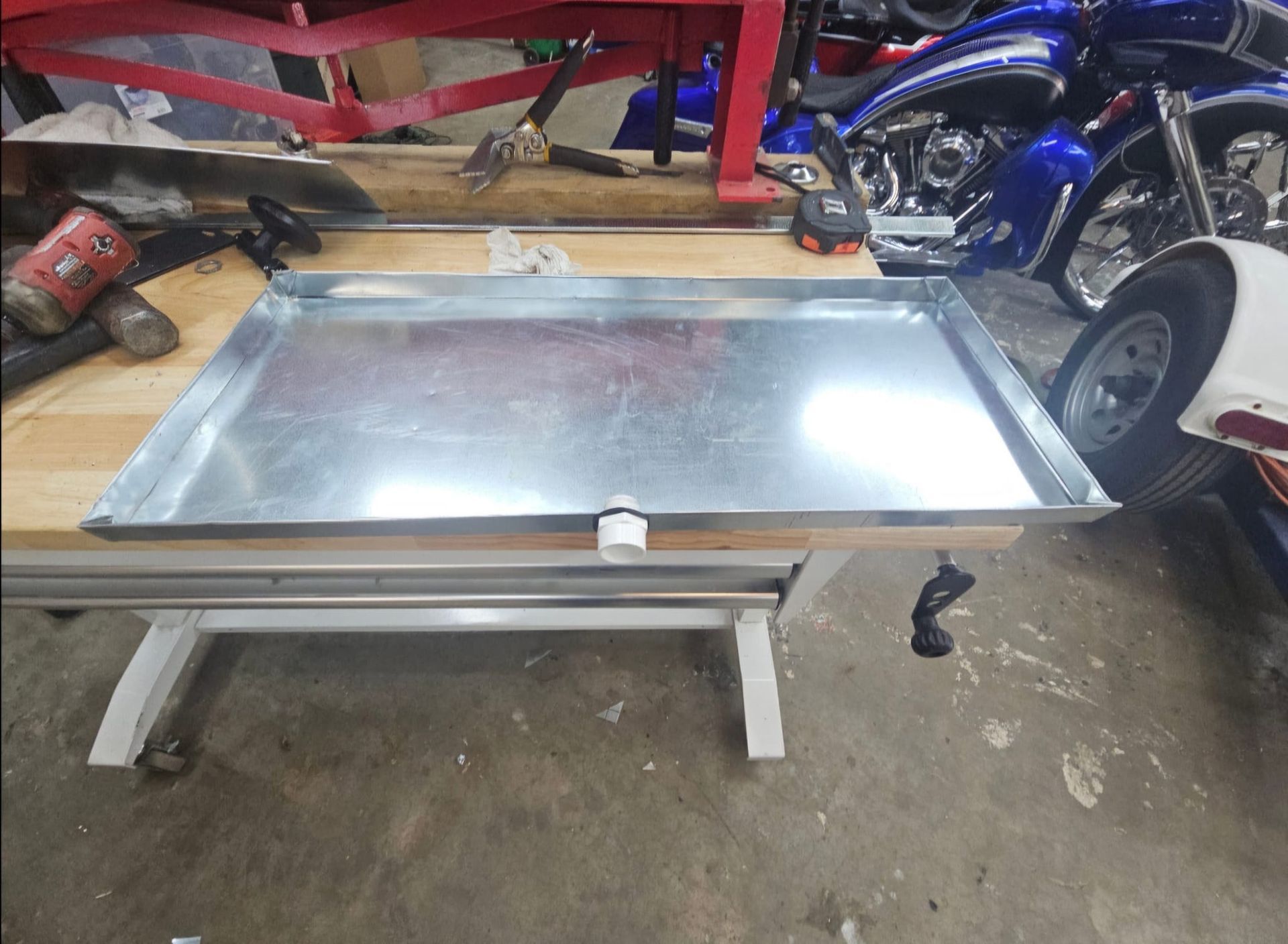 A metal tray sits on a wooden table next to a motorcycle