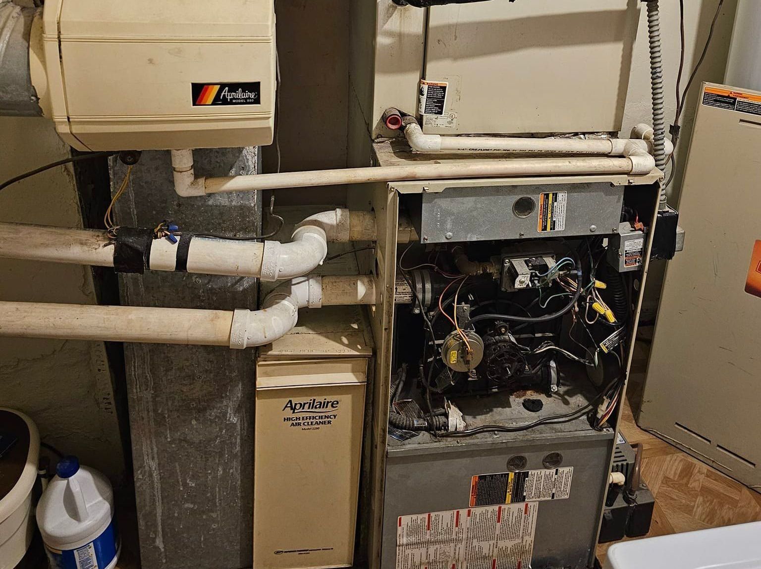 A broken furnace is sitting in a basement next to a bucket of bleach.
