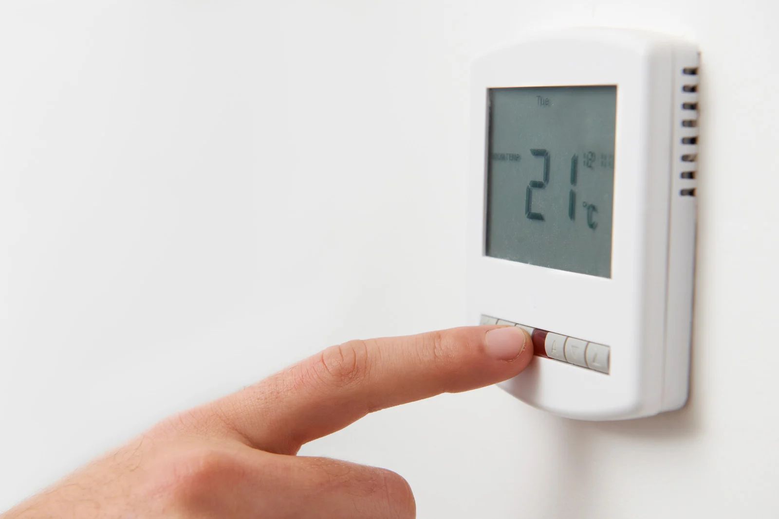 Hand adjusting thermostat, displaying 21°C on a white wall.