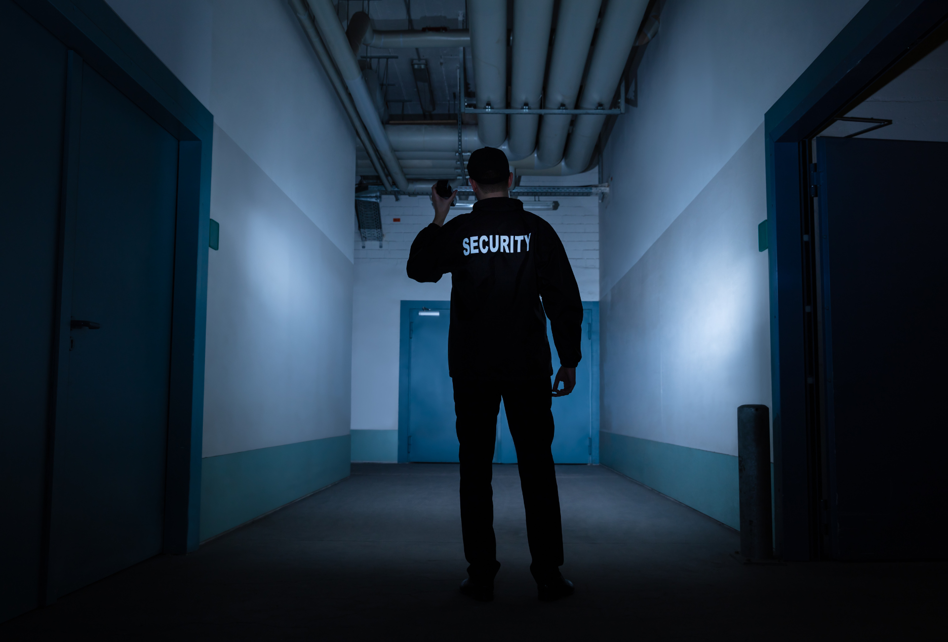 A security guard is standing in a dark hallway holding a flashlight.