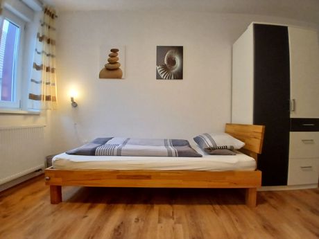Schlafzimmer mit einem Holzbett, gemusterter Bettwäsche und einem weiß-schwarzen Kleiderschrank. 
