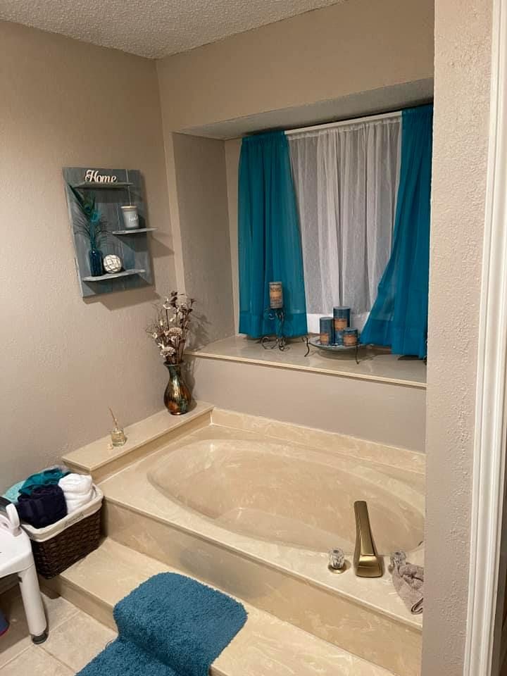 A bathroom with a built-in bathtub, teal curtains, and decorative shelves.