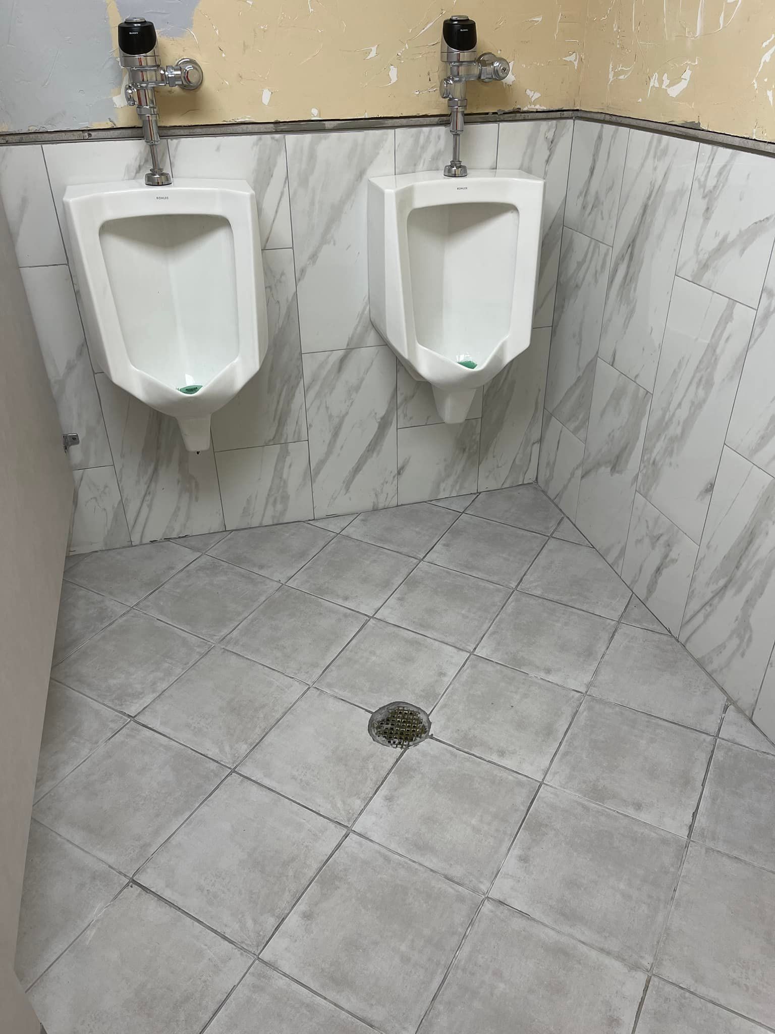 Two white urinals in a public restroom with gray tiled walls and floor.