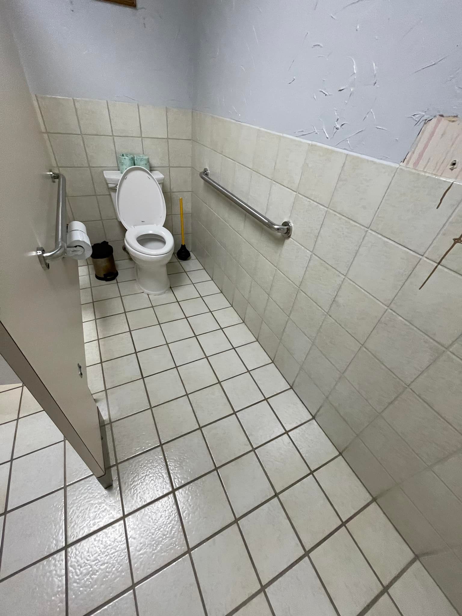 Small, tiled restroom with a toilet, grab bar, and door on the left.