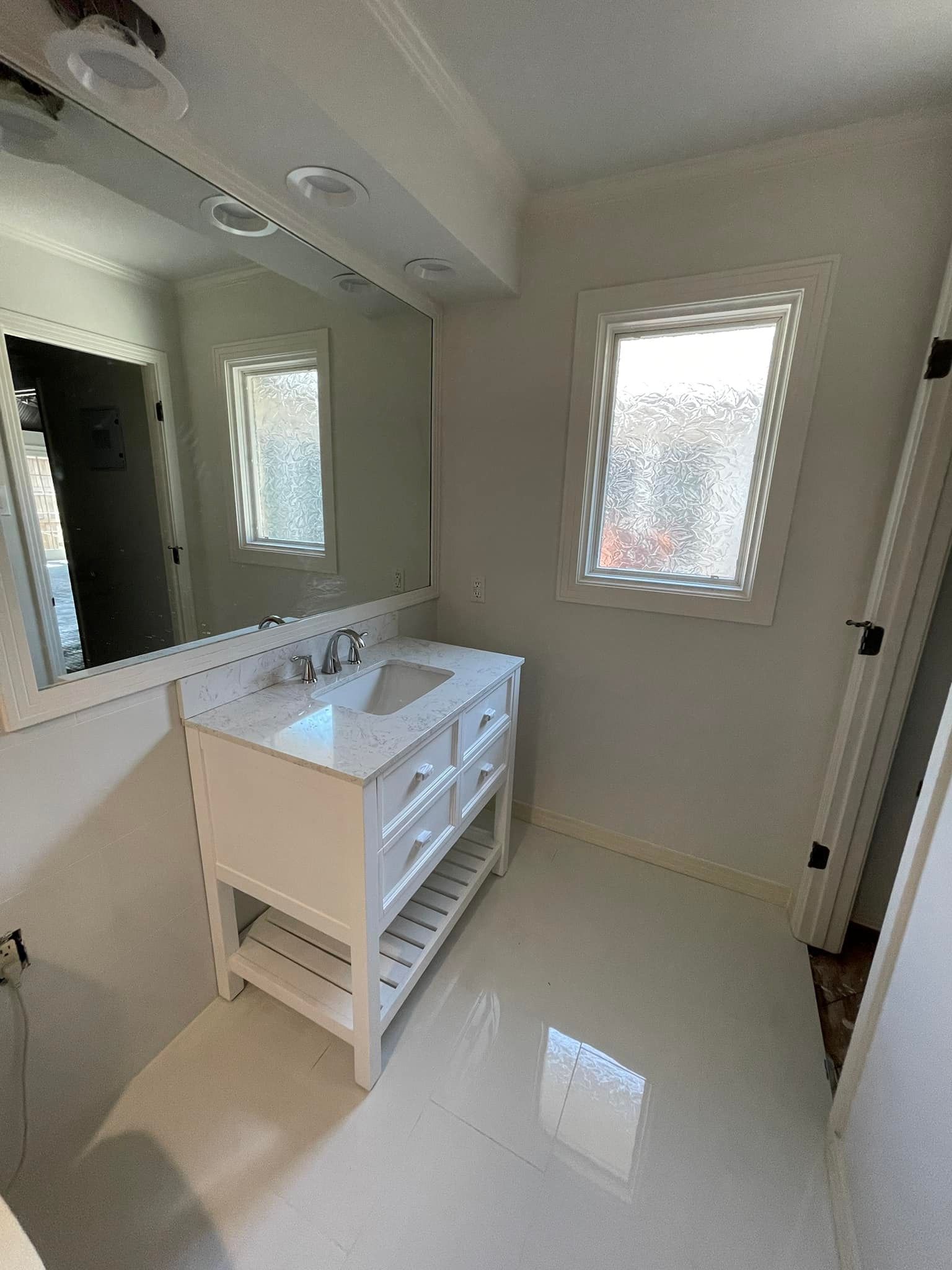 White bathroom with vanity, large mirror, and window with frosted glass.
