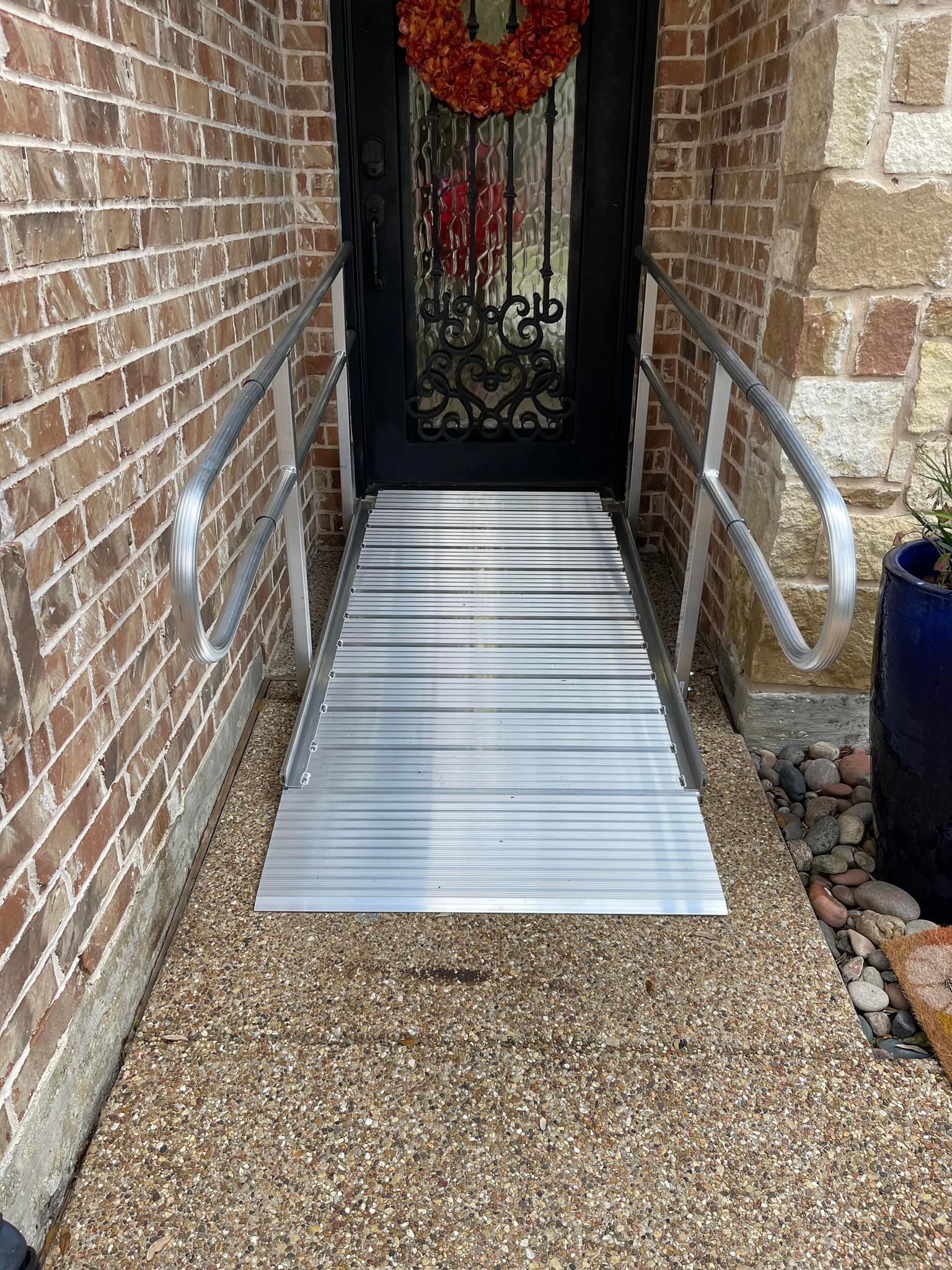 Ramp leading to a front door with handrails, set on a bed of pebbles; brick and stone exterior.