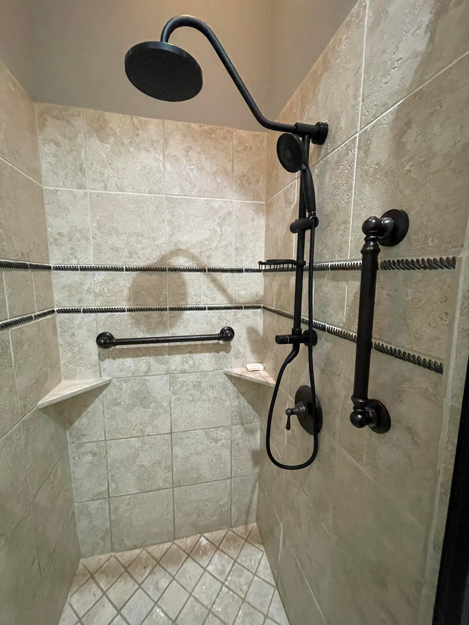 Accessible shower with black fixtures, grab bars, and built-in shelves on beige tiled walls.
