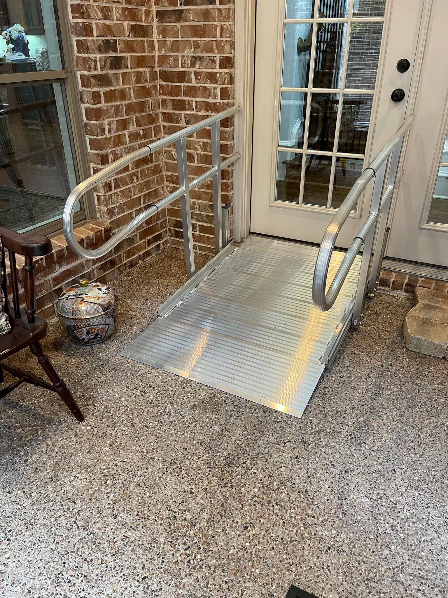 Metal ramp with handrails leading to a glass door. Brick wall background.