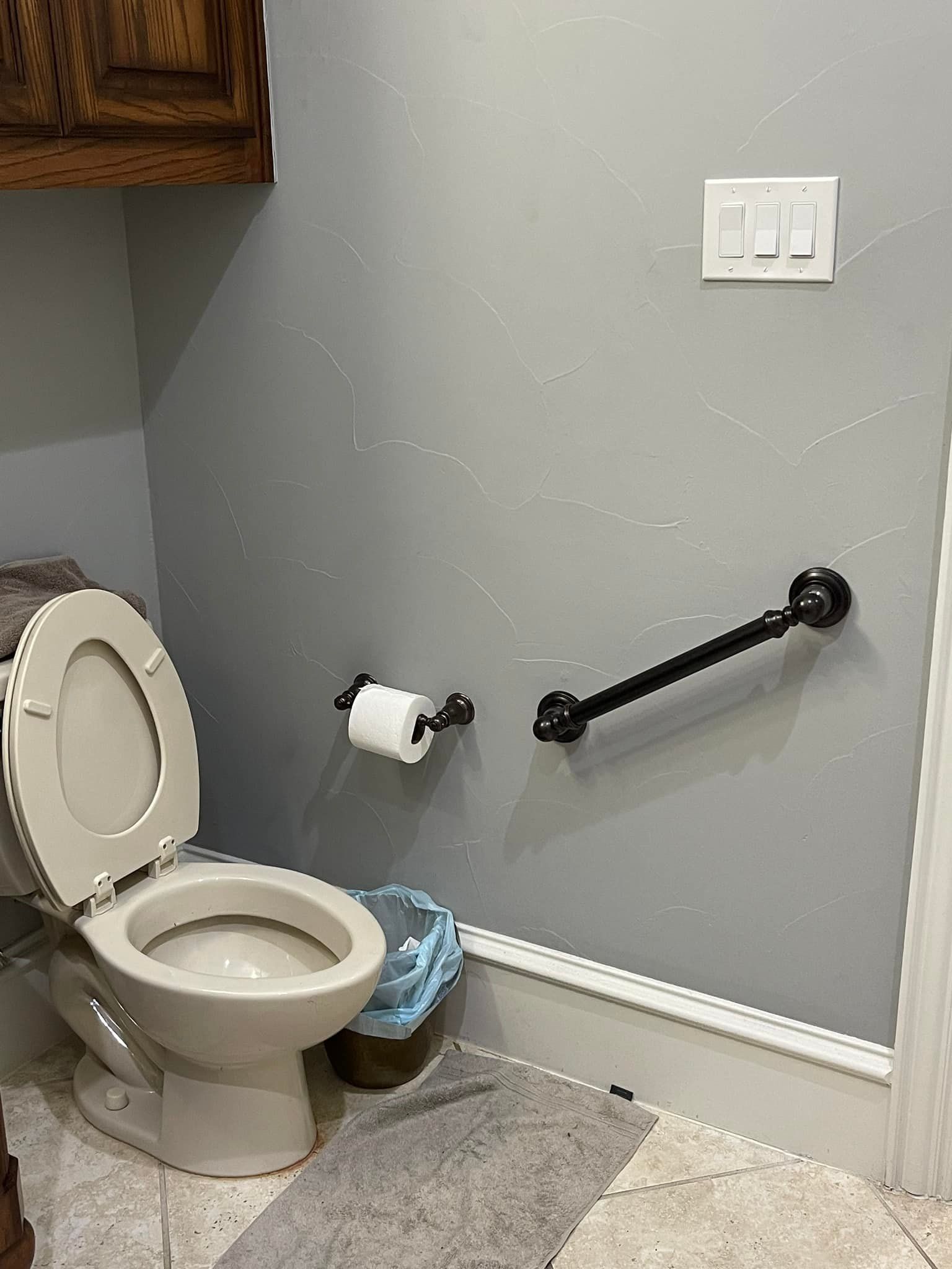 Toilet in a bathroom with a gray wall, grab bar, and tissue holder.