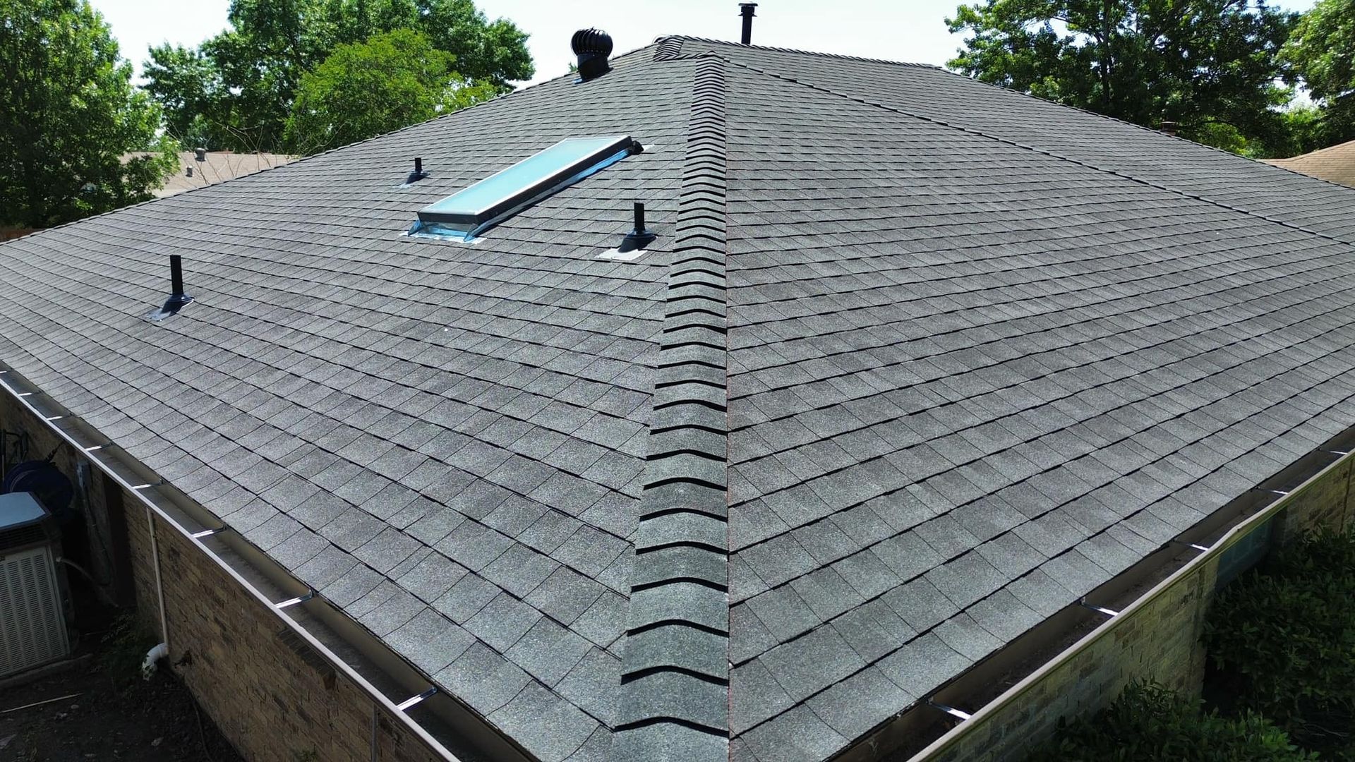 Gray shingled roof with a skylight and multiple vents, viewed from above.