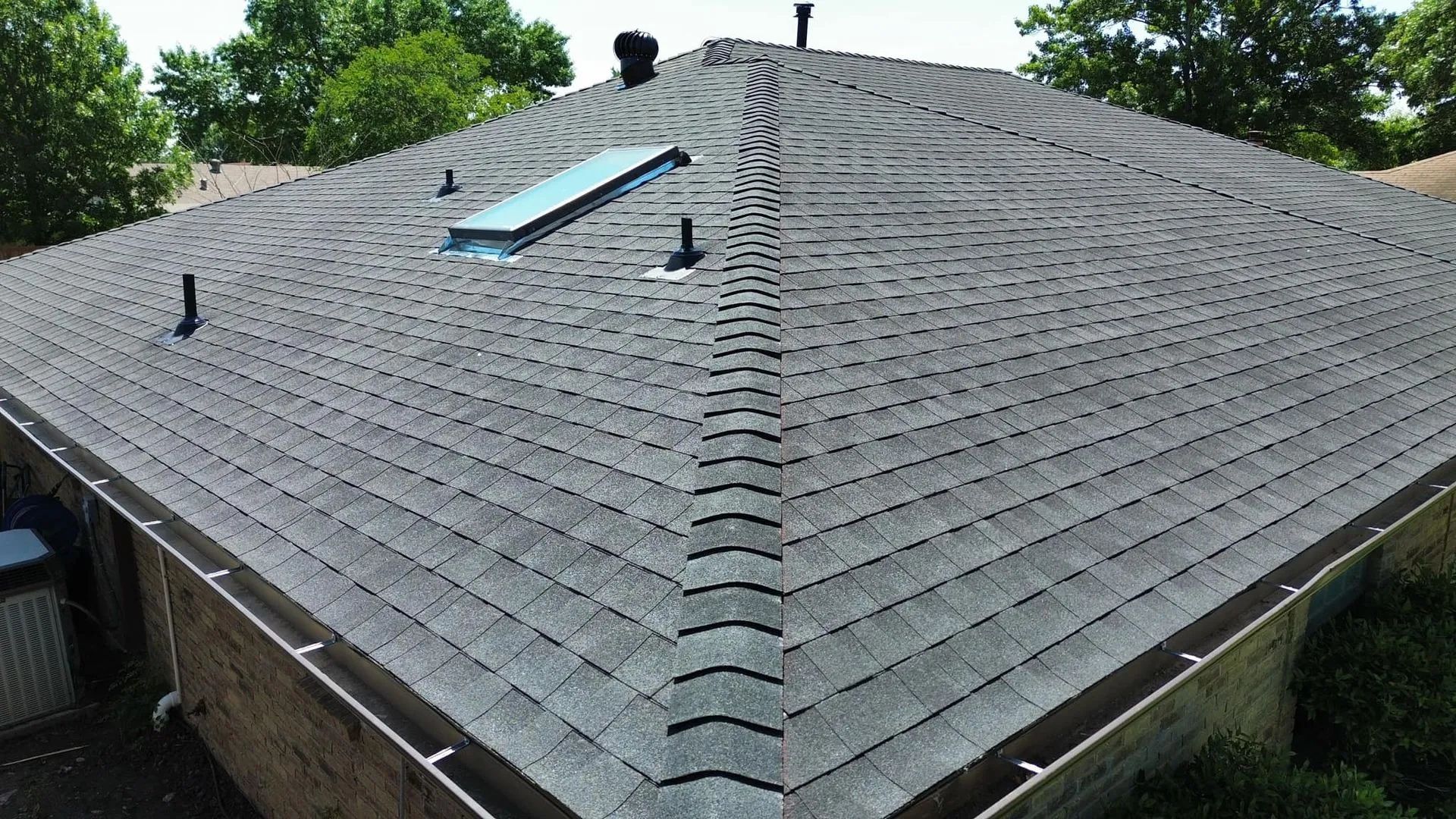Gray asphalt shingle roof with a skylight and vents, viewed from above.