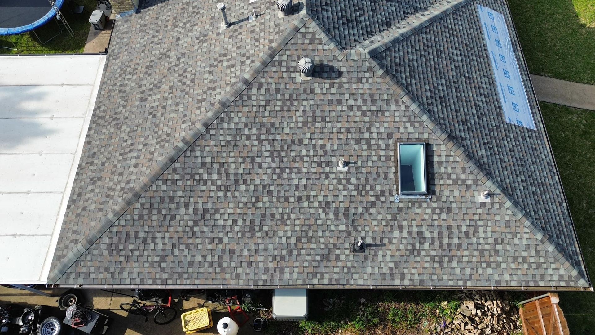 Overhead view of a house roof with grey shingles, a skylight, and white covered area on the left.