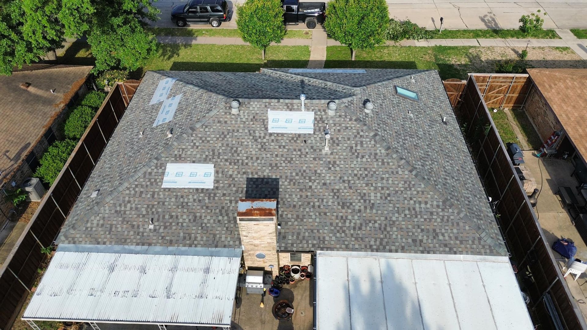Aerial view of a house with a gray shingled roof; brown brick chimney.