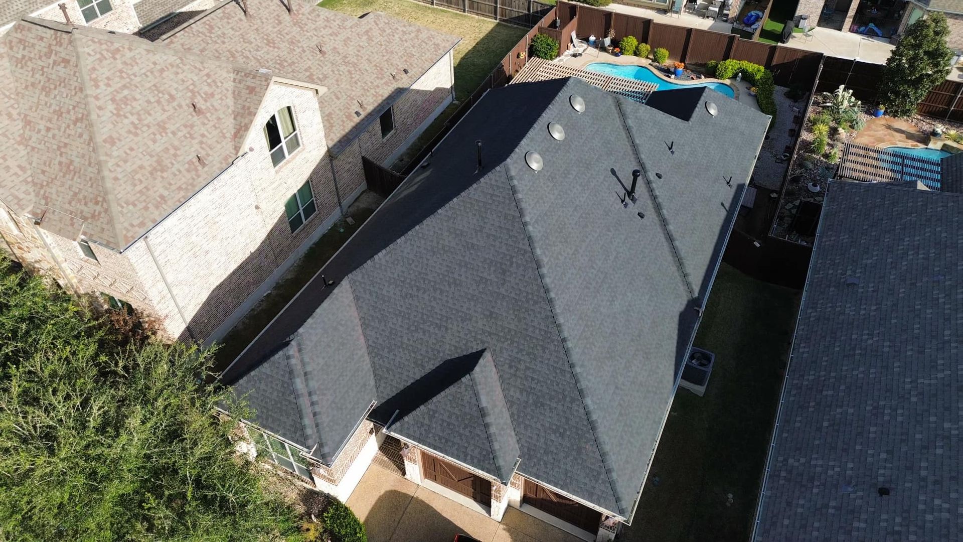 Aerial view of a house with a dark roof, a pool in the backyard, and trees.