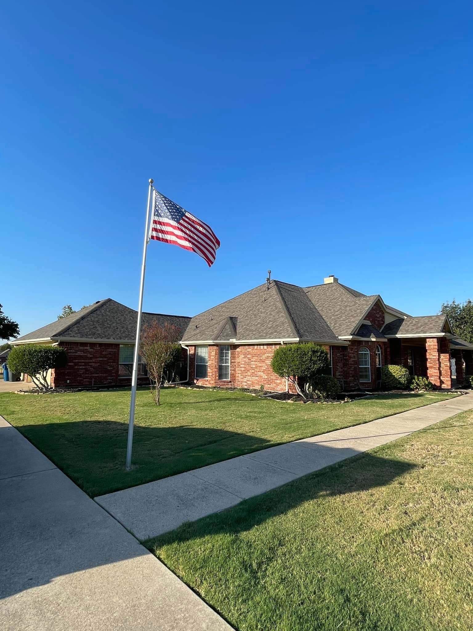A brick house with an American flag waving on a pole, on a sunny day.