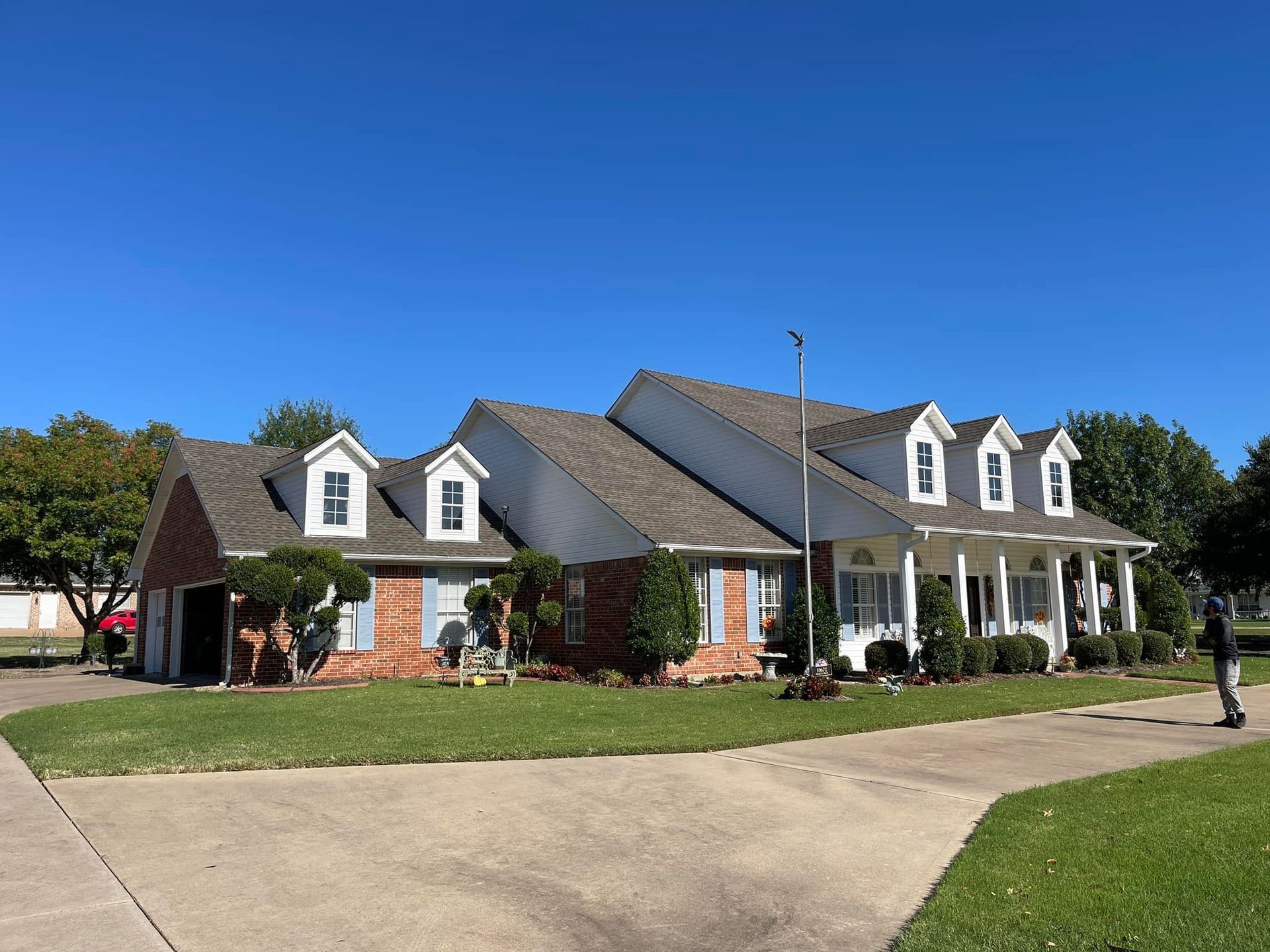 A two-story brick home with a porch and dormers, on a sunny day.
