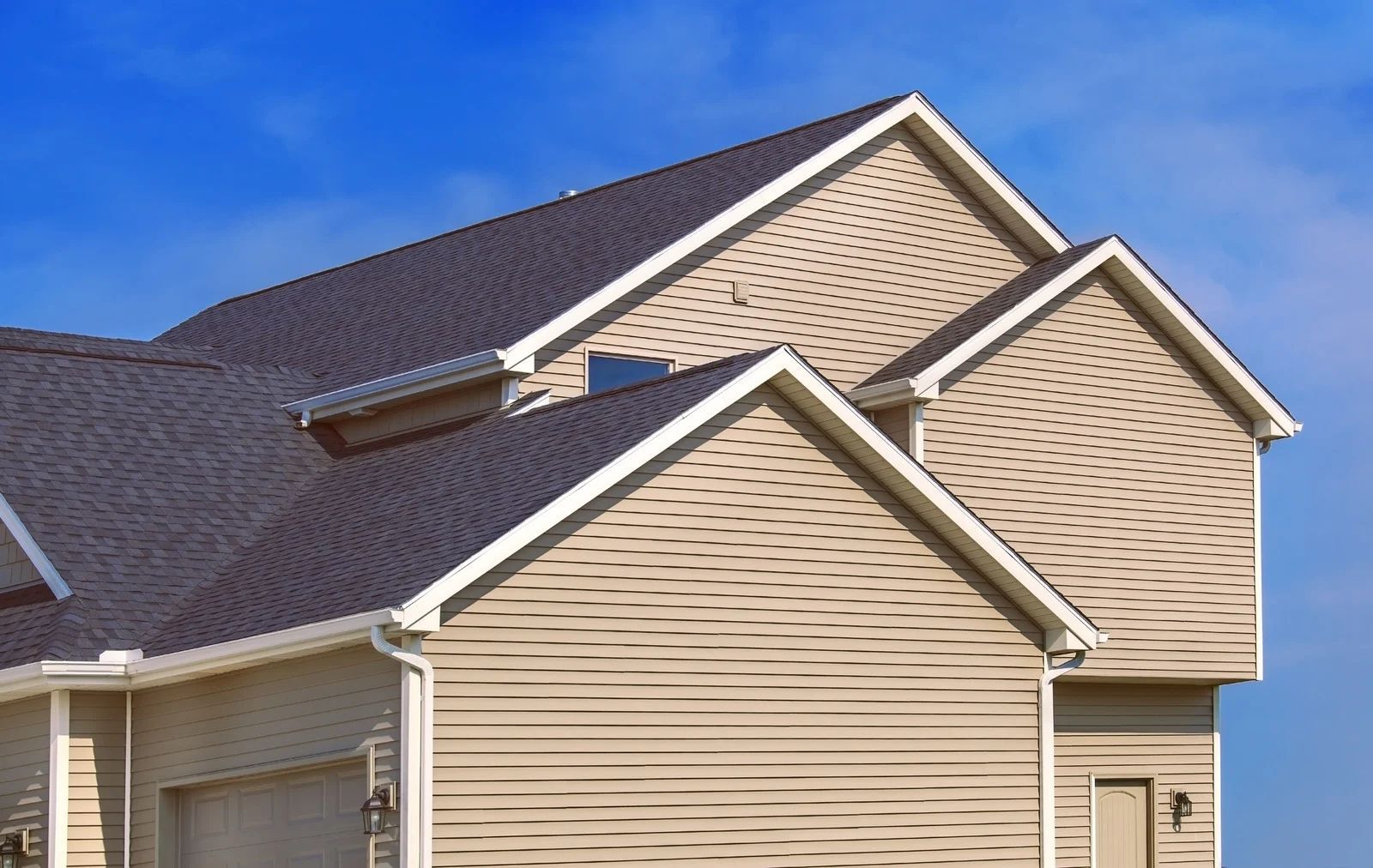 Tan house exterior with dark gray roof against a blue sky.