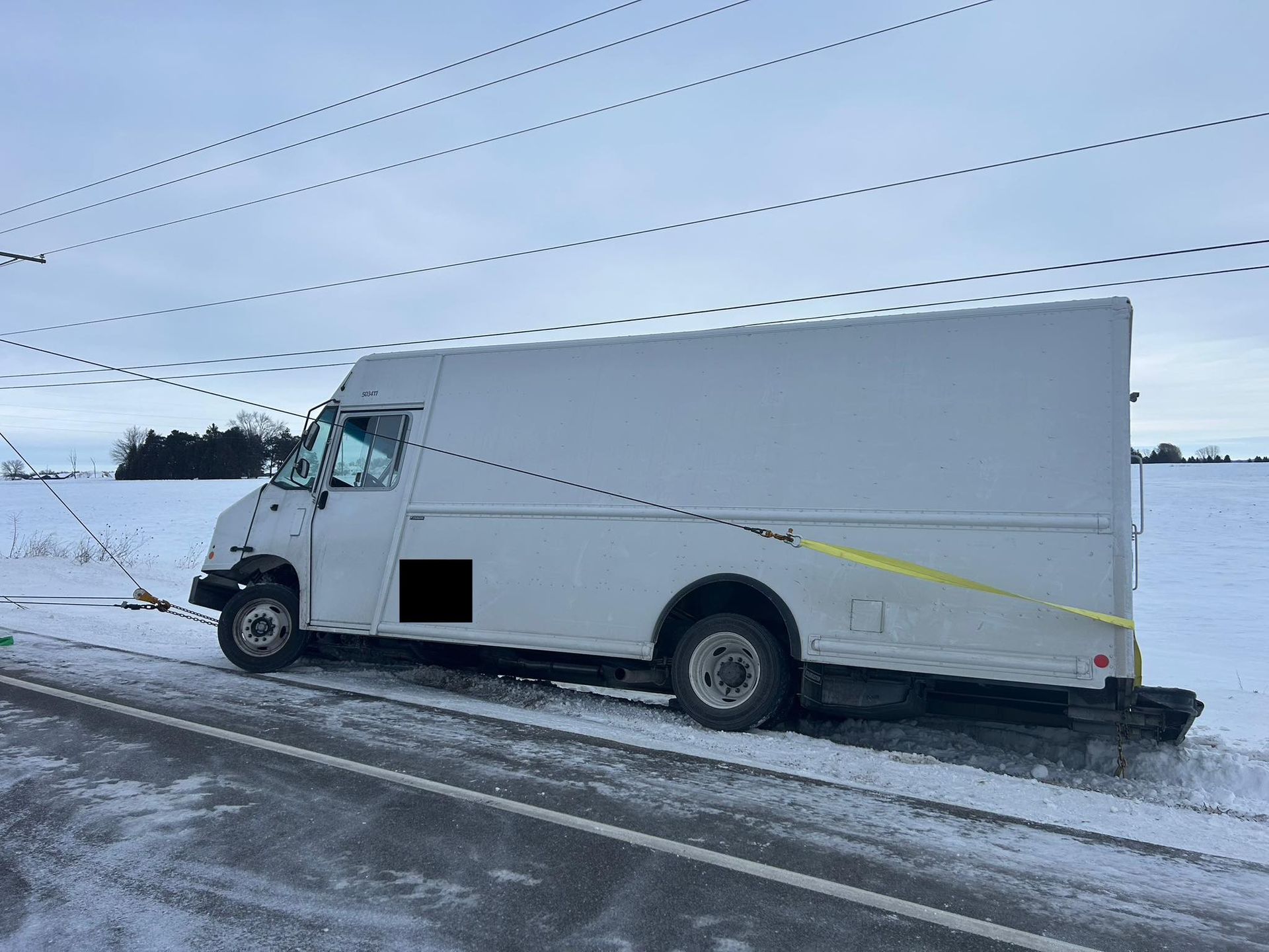 White box truck on snowy roadside, pulled over under power lines.
