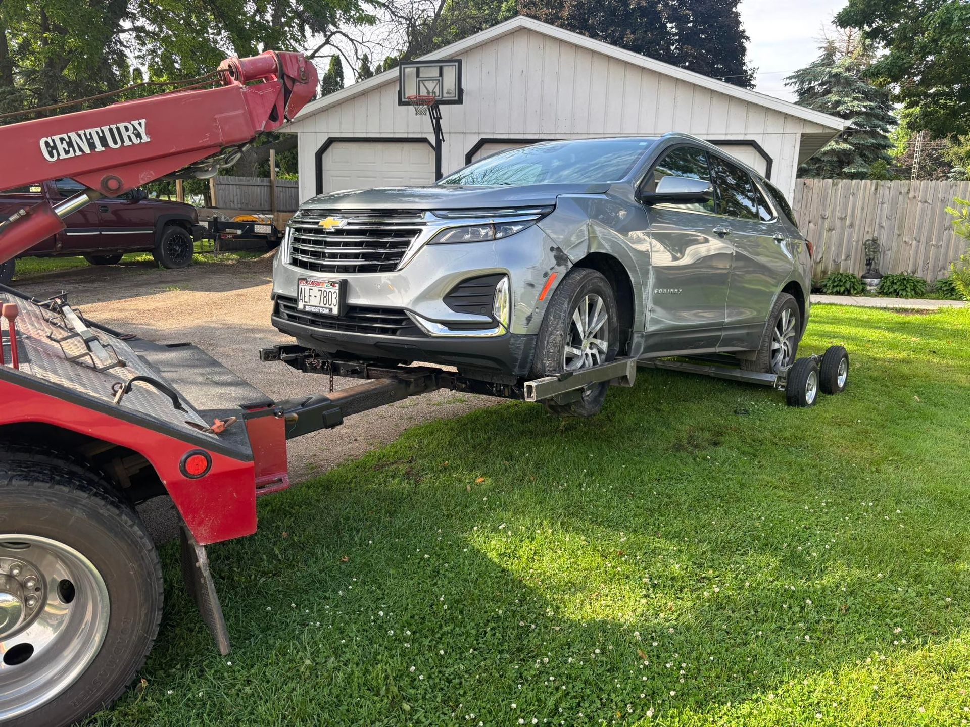 Silver SUV being towed by a red tow truck on a green lawn near a white garage.
