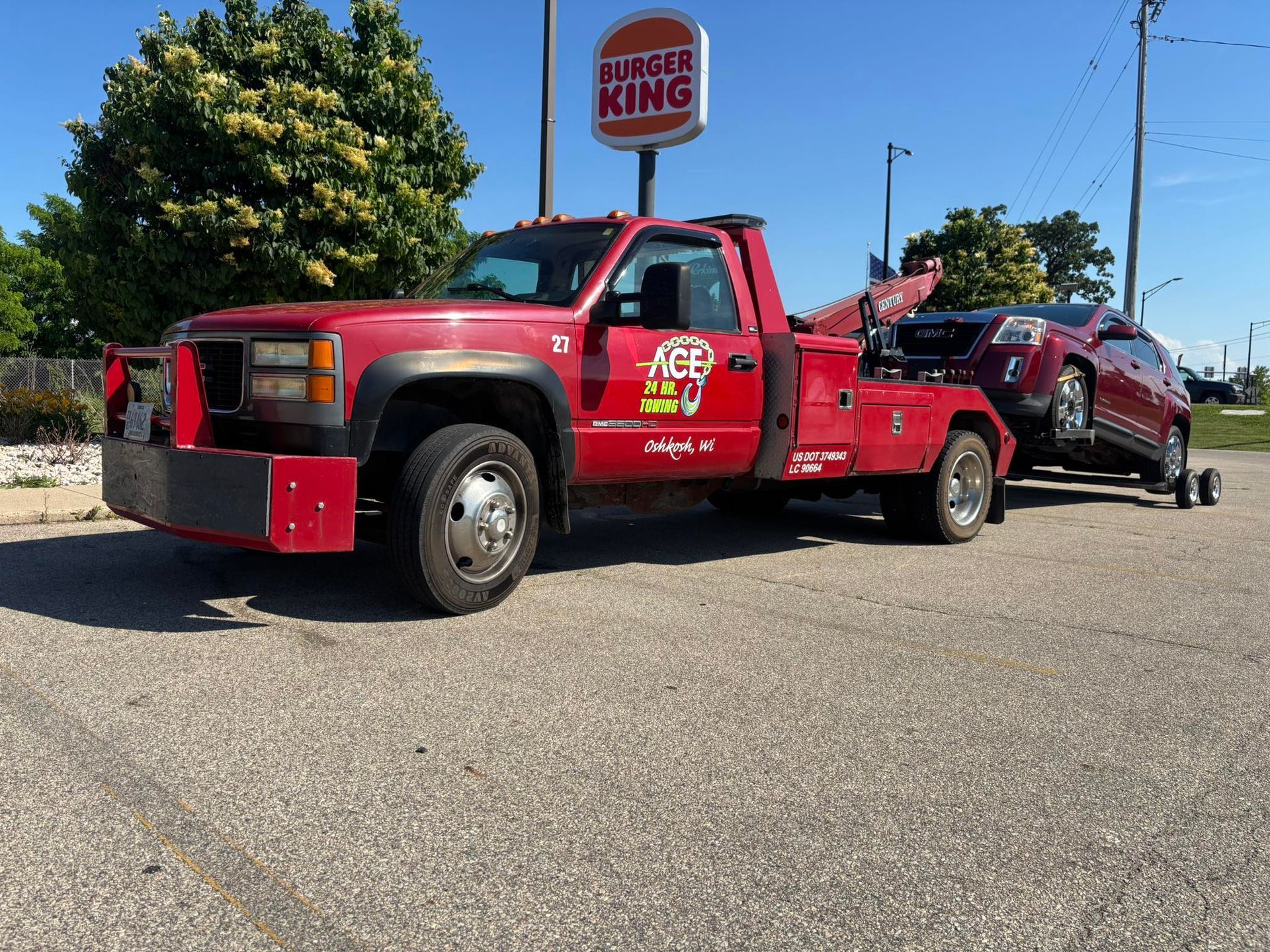 Red tow truck with a vehicle in tow, in front of a Burger King restaurant.