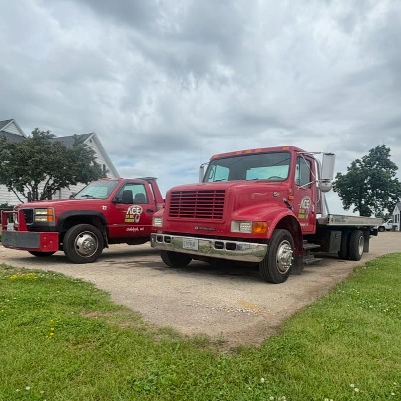 Two red trucks parked on a concrete pad; a smaller pickup truck and a larger flatbed truck. Cloudy sky background.