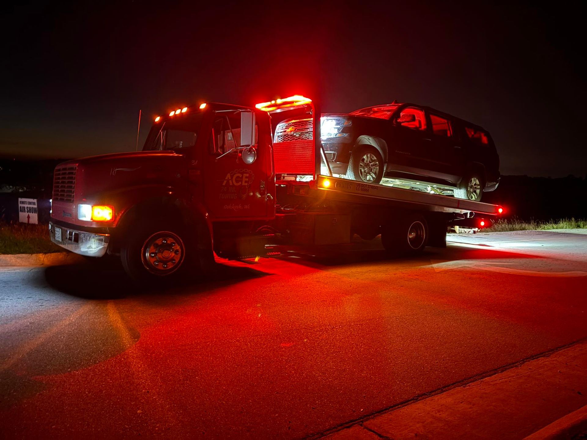 Tow truck with flashing red lights carrying a dark car at night.