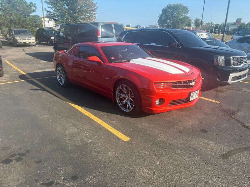 Red Chevrolet Camaro with white stripes parked next to a black SUV in a parking lot.