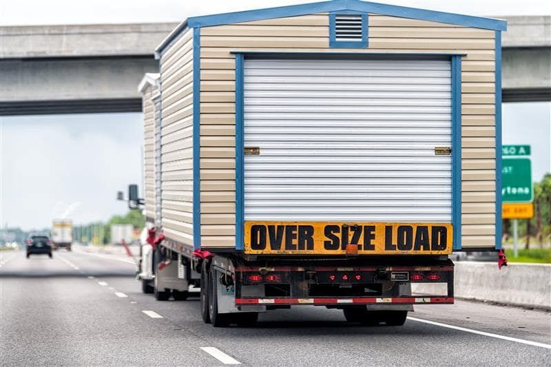 Oversize load truck on highway, carrying a tan and blue building; 