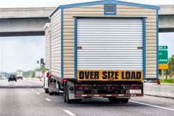 Oversize load truck on highway, carrying a tan and blue building; 