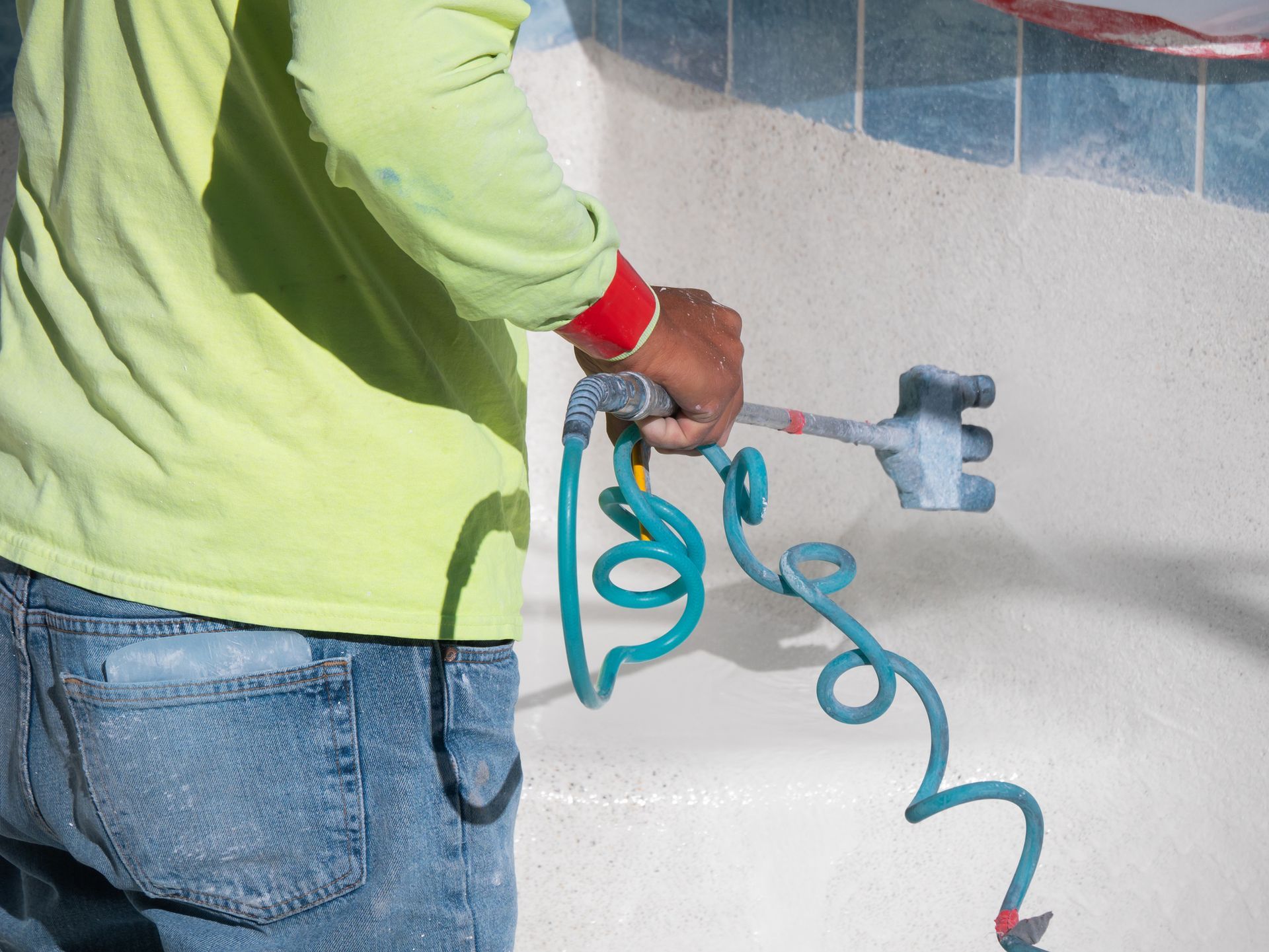 Heritage Pool Plastering renovates a pool with freshly applied cement being watered down by a worker.