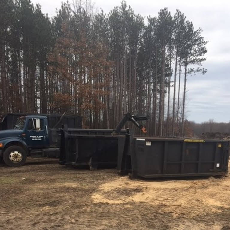A blue truck with two large black dumpsters in a wooded area.
