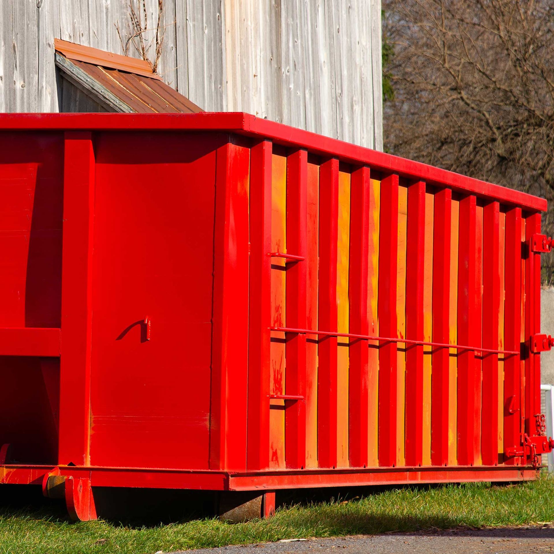Red dumpster in front of a weathered gray wooden building.