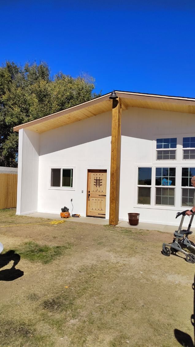 White building with wooden door and pillar. Blue sky, grass yard.