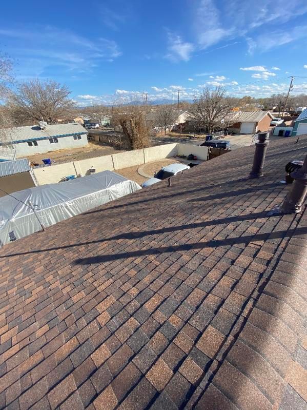 A view from a roof showing brown shingles, blue sky, and neighborhood houses.
