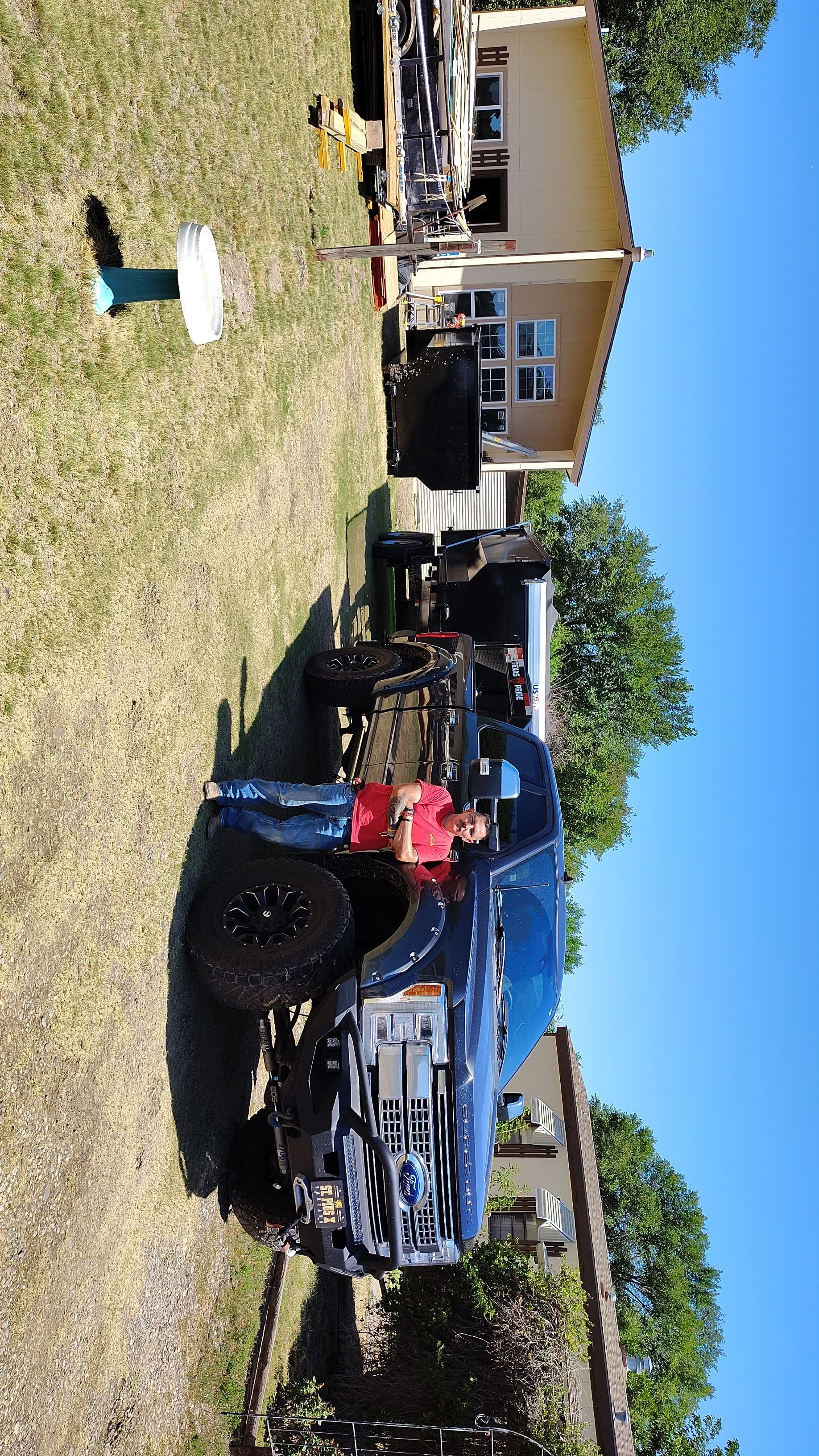 A dark blue pickup truck parked on grass, person near it, sunny day. Houses in the background.