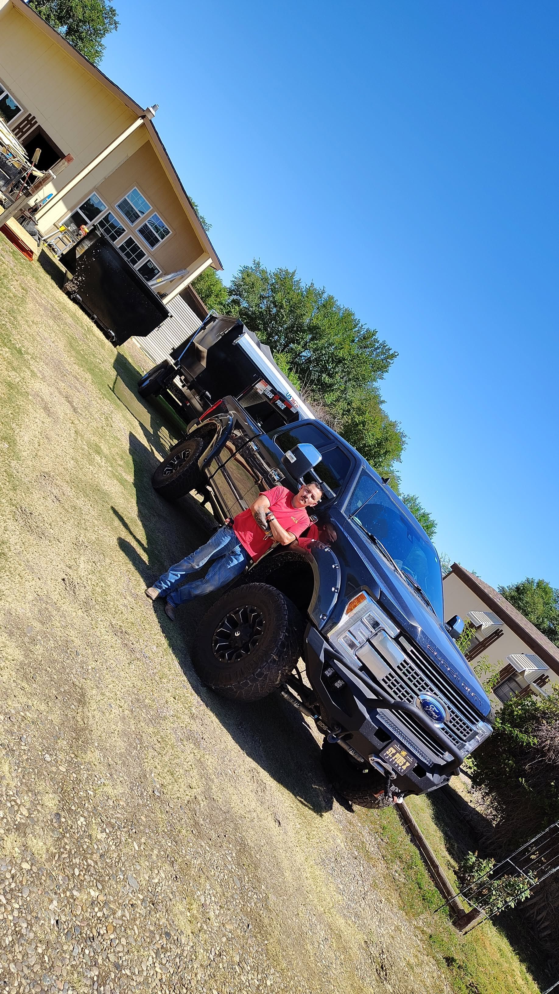 Person in a red shirt standing next to a black pickup truck, outdoors on a sunny day.