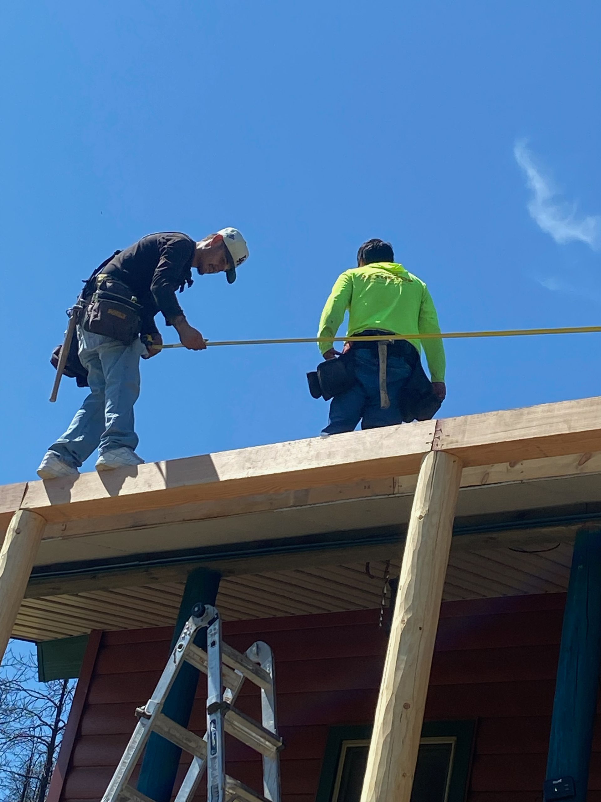 Two construction workers on a rooftop, securing a beam, under a clear blue sky.