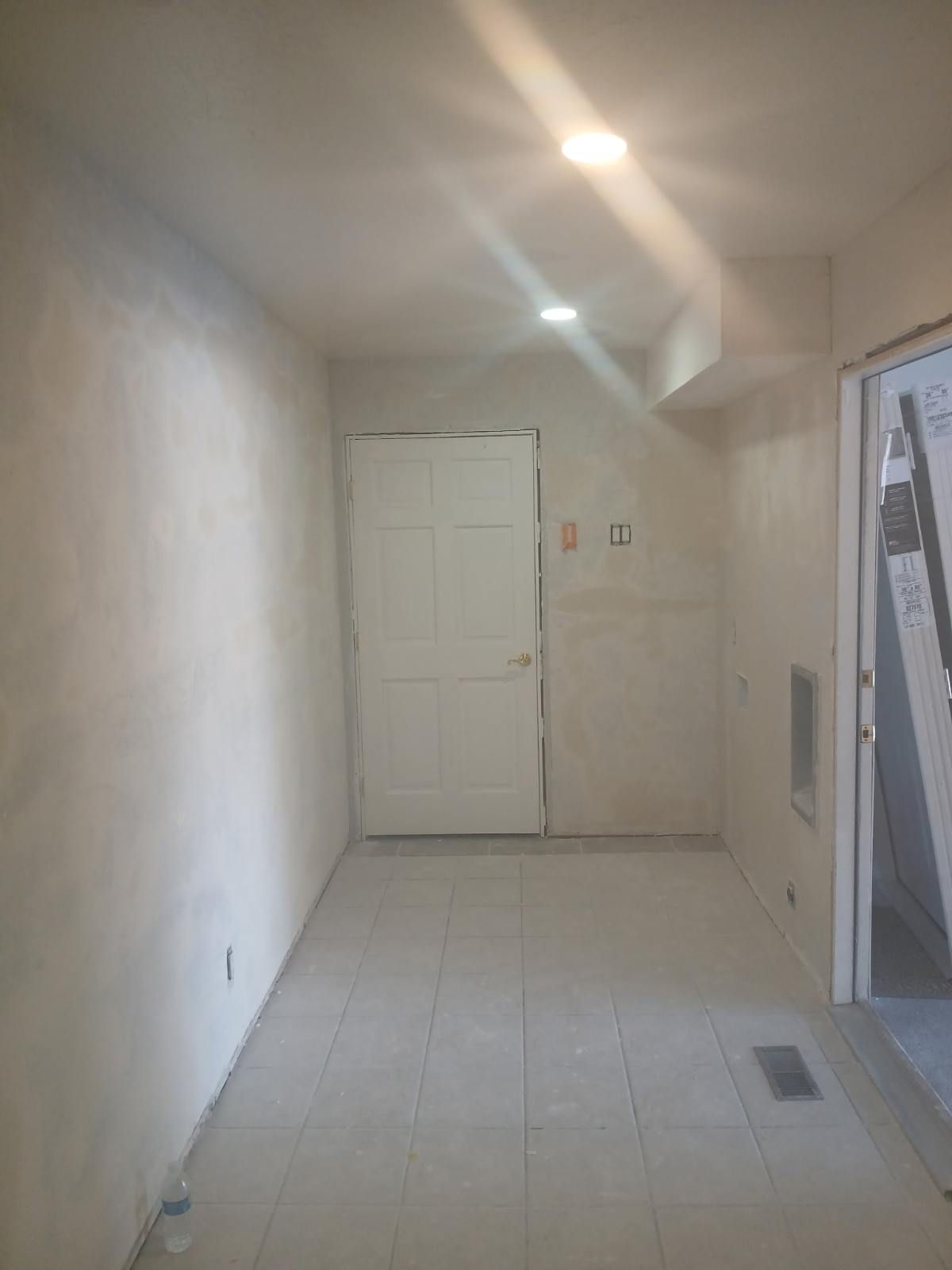 Small room with white walls, a white door, and tiled floor; under construction.
