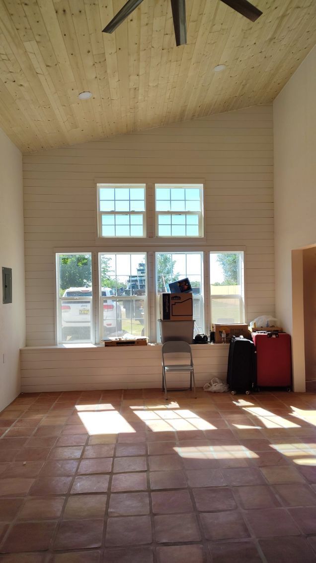Interior of a room with large windows, white walls, and wood-plank ceiling. Terra cotta floor.